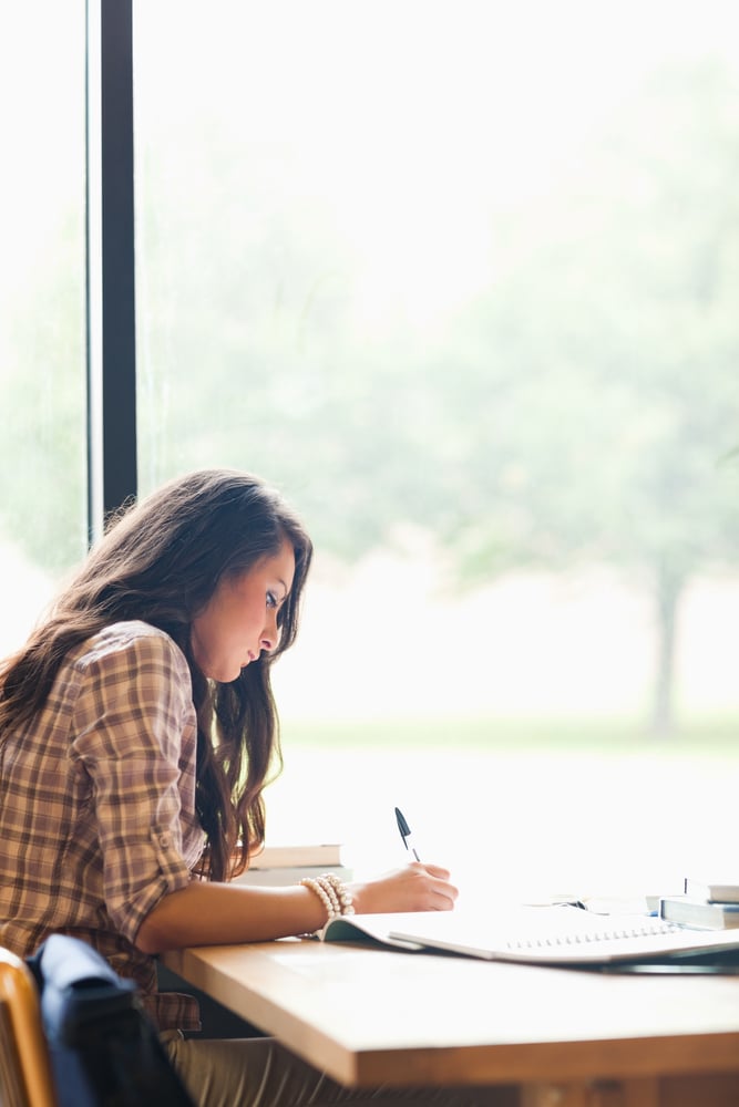 Portrait of a serious young student writing an essay in a library